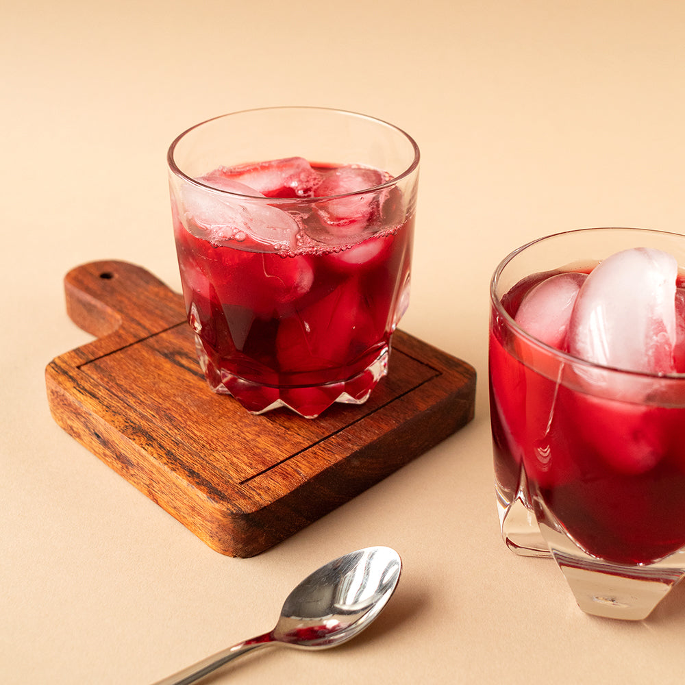 Two short glasses of iced herbal tea, one on a serving board.