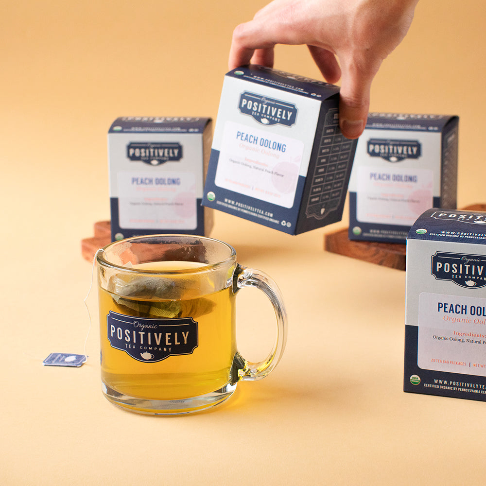 A mug of brewed Peach Oolong tea in front of several tea boxes, some on serving boards.