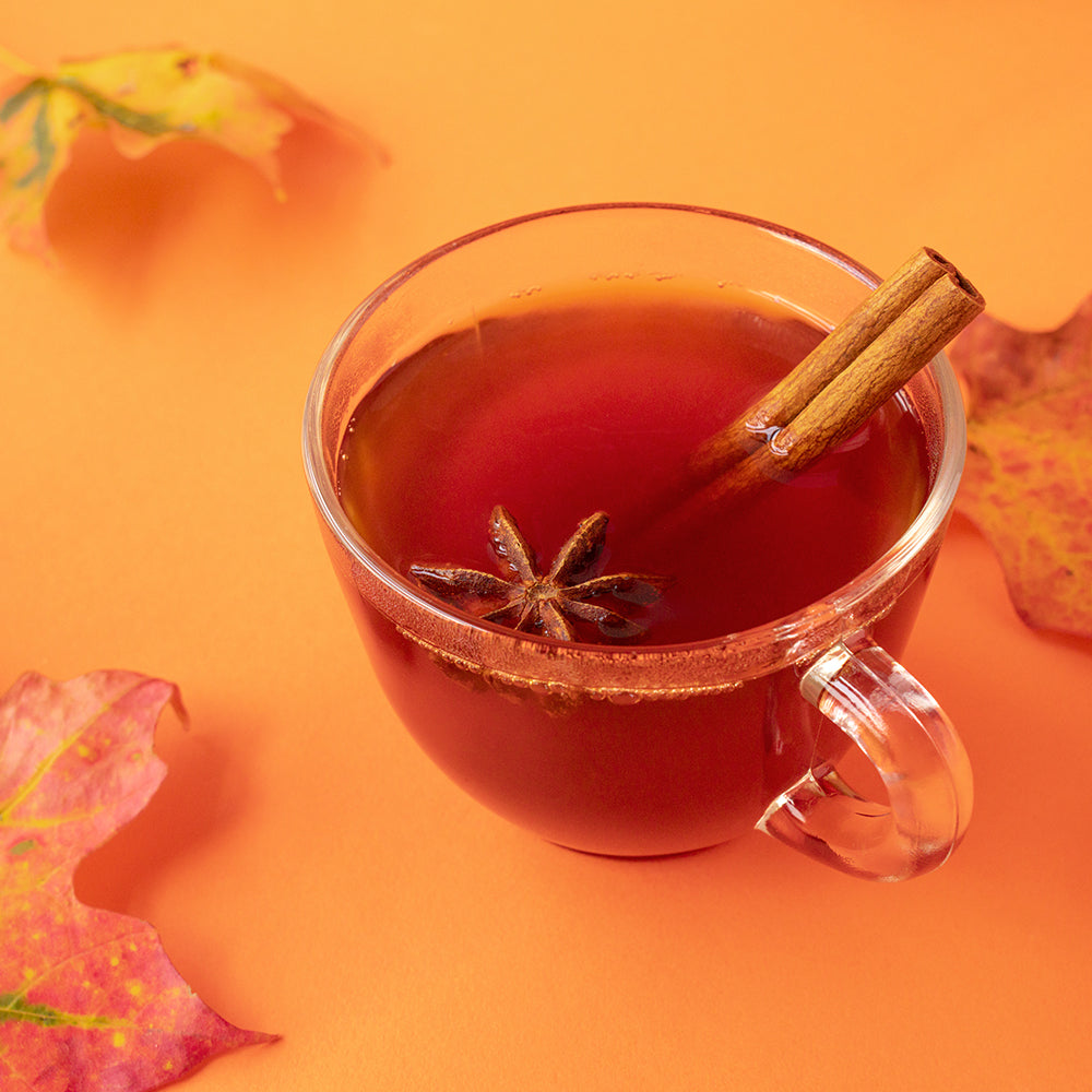 A cup of Wisdom Pu-Ehr Chai with a cinnamon stick and anise star in it and several fall leaves around.