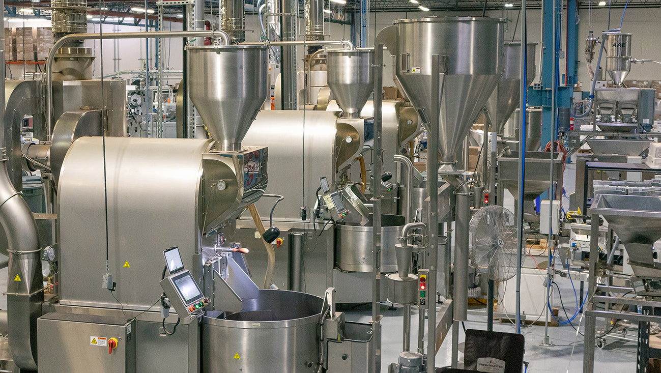 Photograph of coffee production facility with several coffee roasters and hoppers.