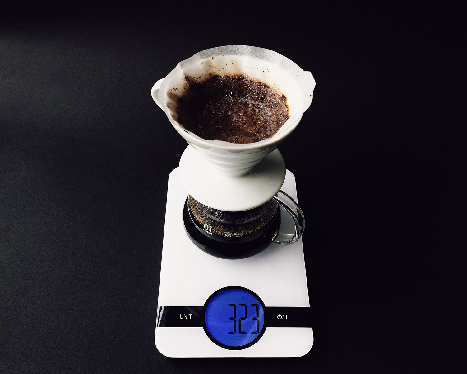 A range server beneath a coffee dripper sits on a white scale against a black background.