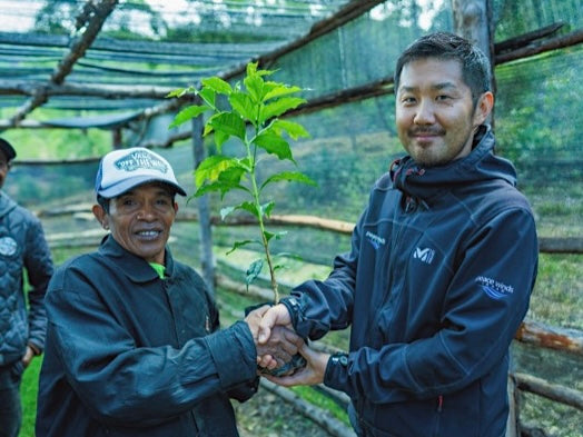 Two coffee producers shaking hands, holding a coffee plant.