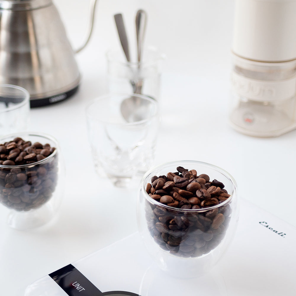 The basic equipment needed to cup coffee: a kettle, weighing scale, burr grinder, a few soup/cupping spoons, two to five vessels of the same size, a dip cup full of hot water, and two to five different coffees to cup.