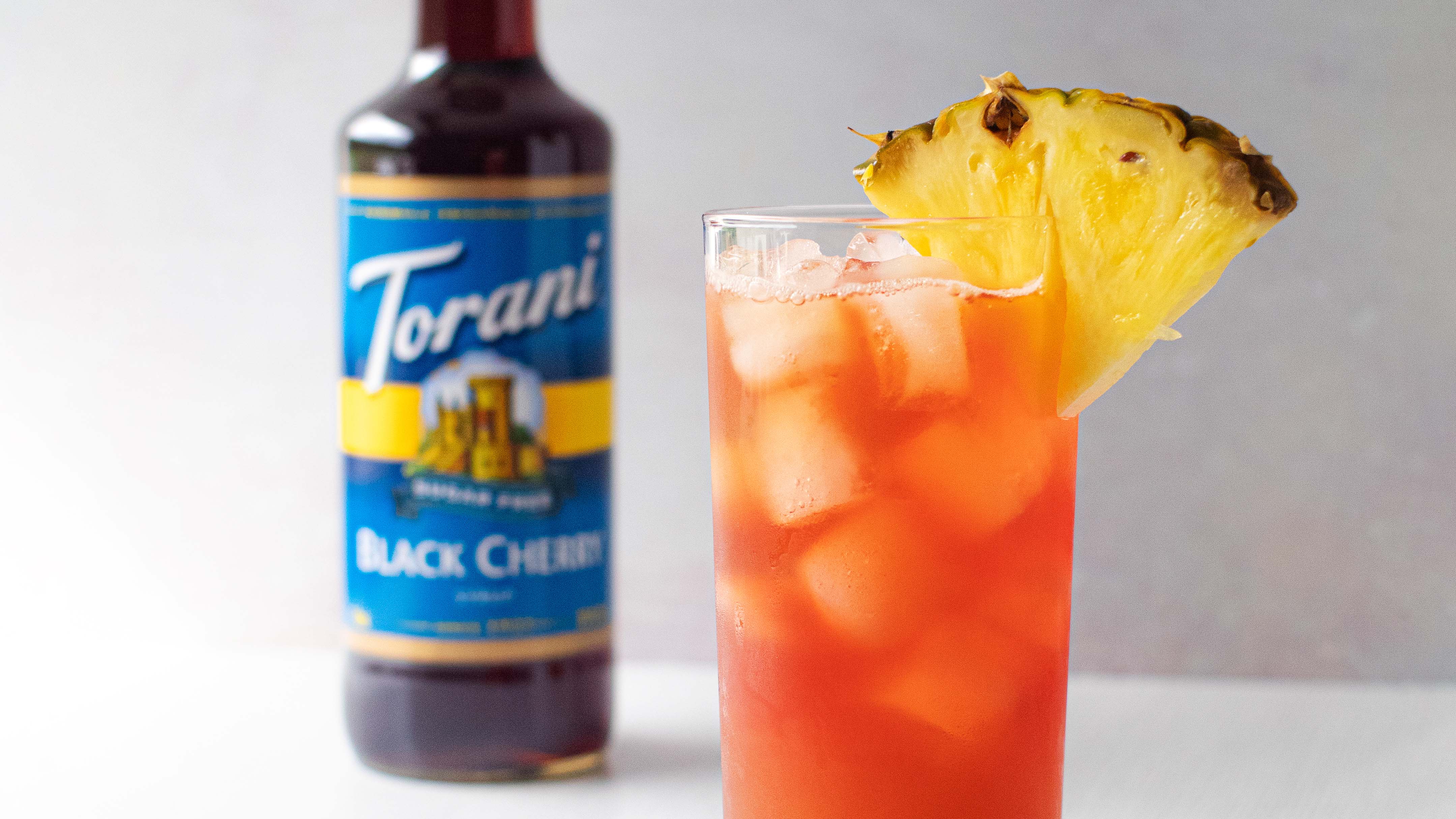 A glass of iced tea with a pineapple triangle and a bottle of flavored syrup.