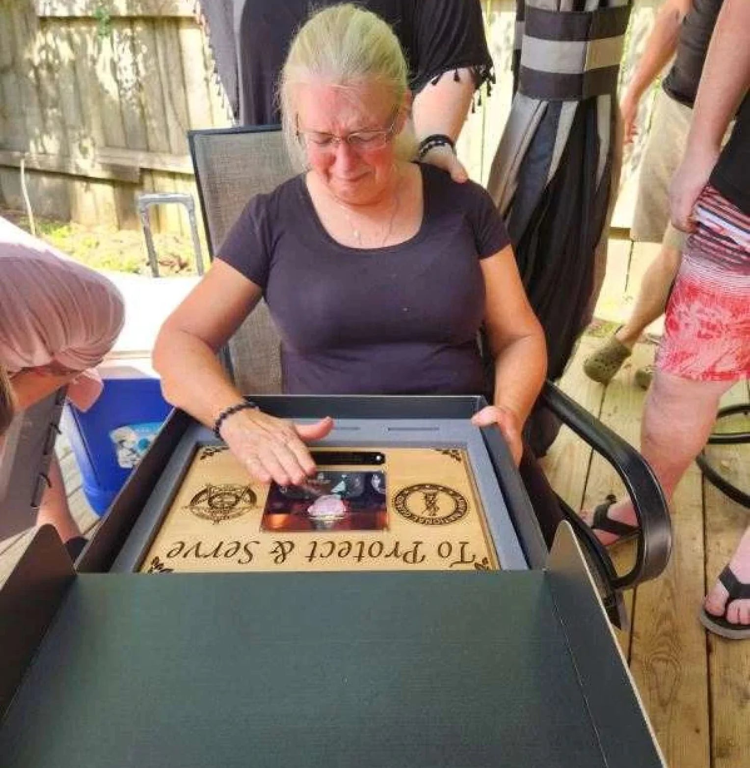 A woman is tearfully opening a heartfelt gift surrounded by friends or family.