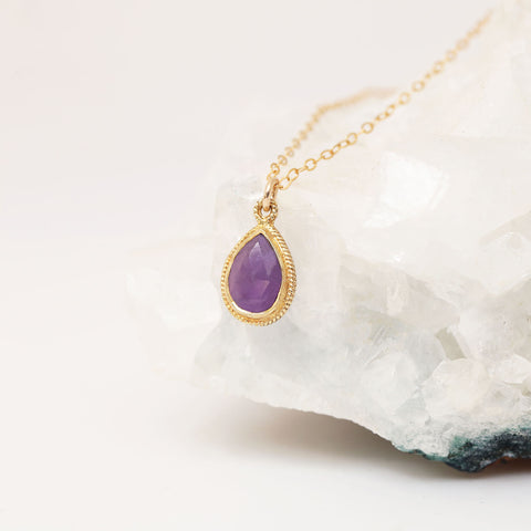 close up of amethyst pendant on gold chain dangling on white crystal; shown from the side