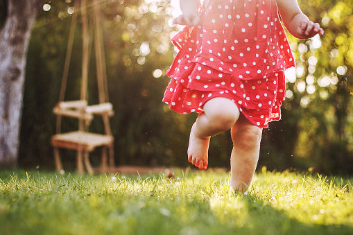 Toddler in red dress running through grass with bare feet.