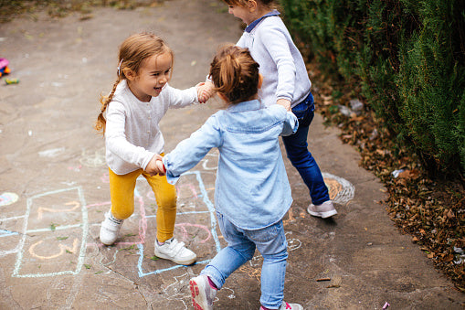 Three children holding hands around a hopscotch drawn with chalk