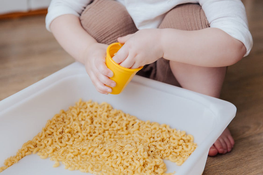 child scooping pasta from a bin with a cup