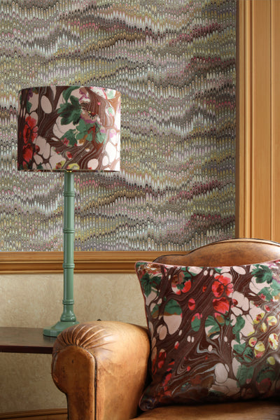 Velvet floral cushion on leather armchair with matching velvet lampshade and patterned wallpaper