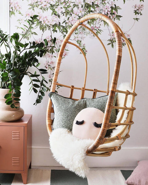 A natural colored rattan hanging chair hung from the ceiling in a girls room