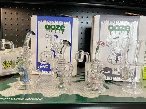 4 mini dab rigs are lined up on a shelf. They are the Ooze Ocean Series Recycler mini rigs and the Ooze Toxic Barrel Quartz mini rig.