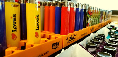 A row of assorted Bic lighters is on a shelf in a convenience store