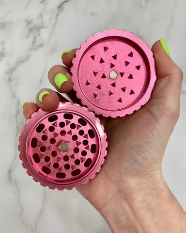 A female hand with green nails holds a pink Ooze Saturn grinder fully open, both sides held in one hand above a white marble background.