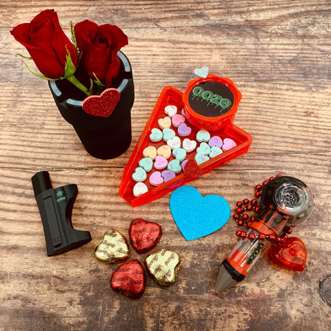 The Ooze Valentine's His Bundle sits all spread out on a wood surface, surrounded by roses, conversation hearts, chocolate hearts, and a heart necklace