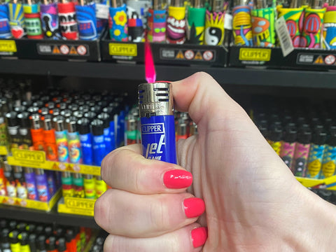 A girl is holding a blue Clipper Jet Lighter and is igniting it to show the jet flame