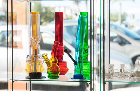 Assorted colored glass bongs are displayed in a window