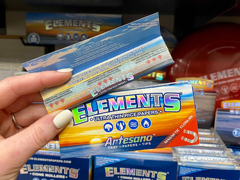 Two packs of Elements rolling papers are held up, one of the packs is open to show the paper inside.