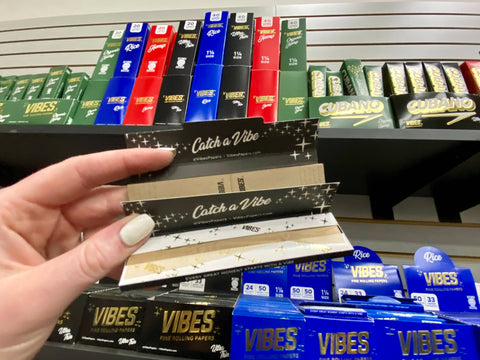 A black booklet of Vibes rolling papers and tips is opened in front of a shelf full of other Vibes rolling papers products in the Cannatron wholesale showroom.