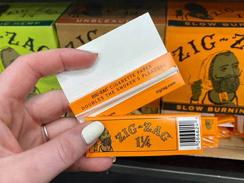 An orignal orange leaves pack of Zig Zag rolling papers is held in front of other Zig Zag paper displays.