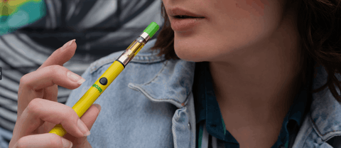 A brunette girl smokes her yellow Ooze Twist Slim Pen 2.0 with an OozeX cartridge