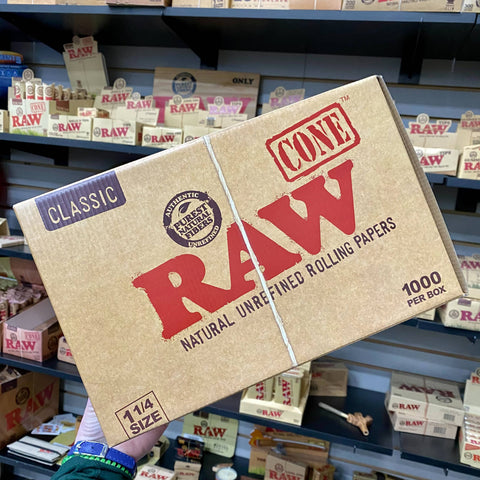 A bulk box of 1,000 RAW cones is held in front of the RAW display wall in the Cannatron wholesale showroom.