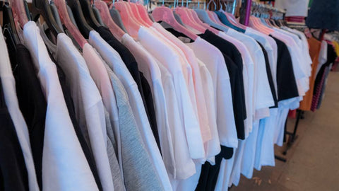 A t-shirt rack in a smoke shop has branded merch on white, gray, and black t shirts.