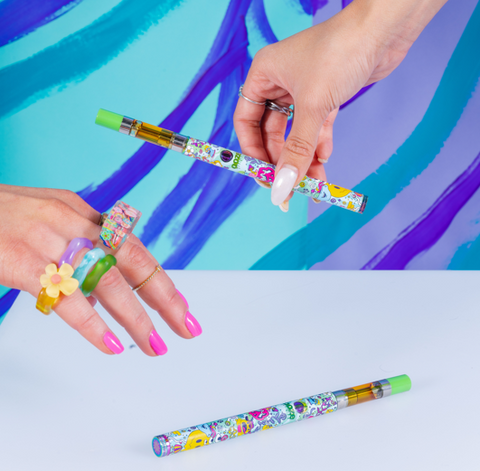 One hand is holding and Ooze Twist Slim Pen 2.0 in the Chroma design, and a second hand is reaching for the same type of vape.