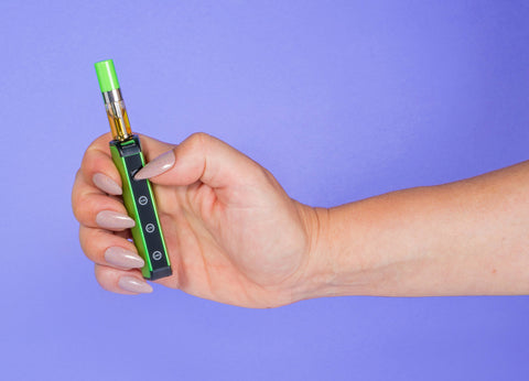 A white girl with long finger nails is holding a green Ooze Novex with an OozeX cartridge inside