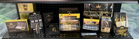 POP Displays filled with different King Palm accessories like smoke clips and ashtrays are displayed on a black shelf in a smoke shop.