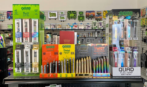 6 different displays of Ooze vape pen batteries are displayed on a smoke shop shelf.