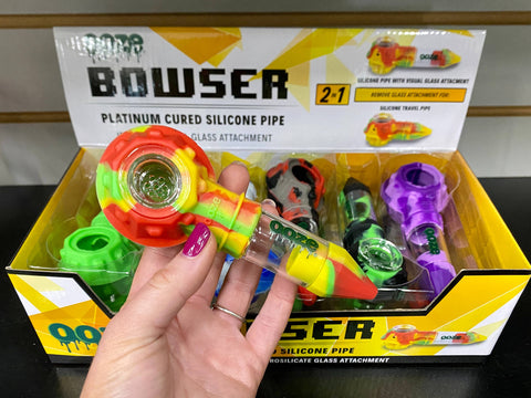 Holding a rasta Ooze Bowser silicone pipe above a 12ct display of the pipes