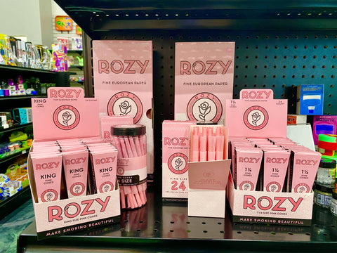 A shelf full of displays of pink Rozy rolling papers, pre-rolled cones, and filter tips