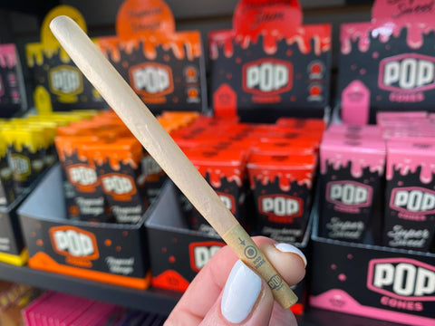 A single Pop Cone is held up in front of the Pop Cone retail displays. You can see where it says to pop the flavor bead on the filter tip.