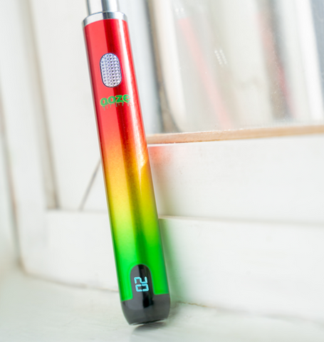 A rasta Ooze Smart Battery is upright with the screen turned on.