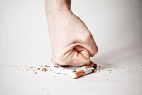 A white male man's hand is in a fist, crushing a pile of cigarettes. Stop smoking tobacco and cigarettes.