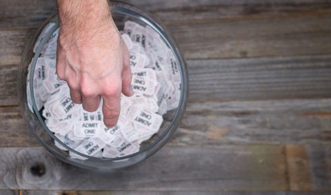 A hand is reaching into a glass bowl filled with white raffle tickets