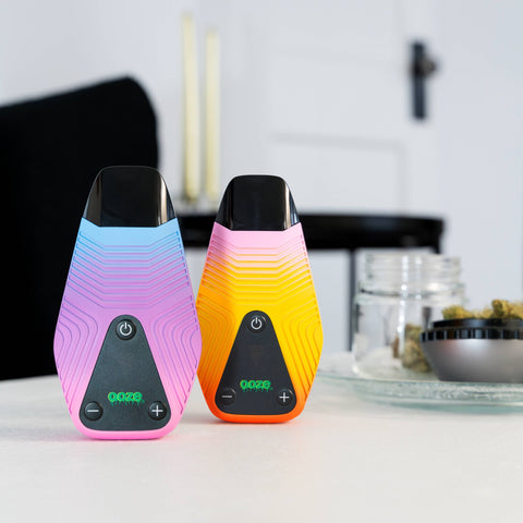 The twilight and sunshine colorways of the Ooze Brink dry herb vape are sitting on a white table in a living room