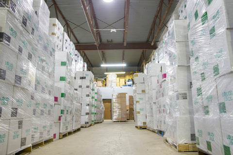 A wide shot of an aisle in the Ooze Wholesale warehouse. You can see both sides are stacked to the ceilings with white Loud Lock boxes on pallets and wrapped.