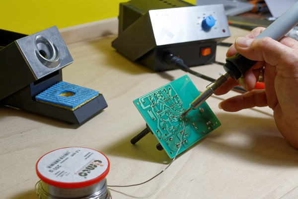 A person doing soldering works on a green circuit board