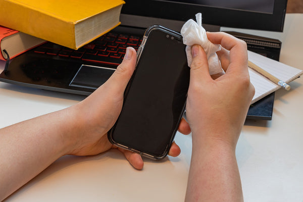 A person cleaning a mobile phone using a wipe