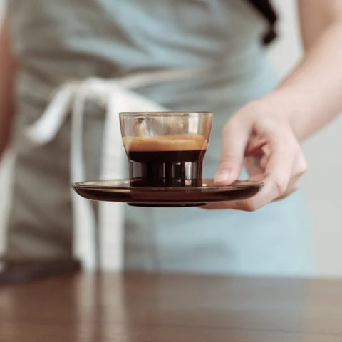 A person holding a cup of roasted coffee, resting on a wooden table, exuding warmth and comfort.