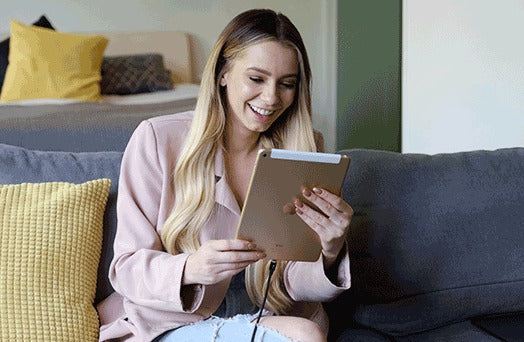 Blonde woman sitting on a couch Facetiming on her gold iPad that's being charged with her Infinity magnetic cable. First universal magnetic charging cable to support 100W PD Charge, QC3.0/4.0 & Data Transfer for Apple, Micro USB, USB C & USB-C Laptops including Macbook Pro.