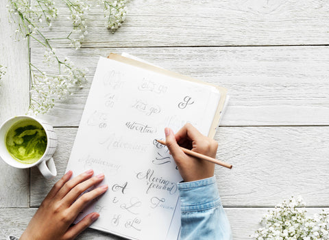 Two hands that are journaling with a green tea on the left side 