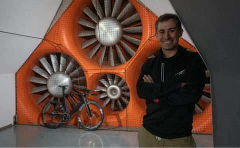 AJ Alley standing with arms crossed in front of the wind tunnel with an A2 Triathlon bike in the background