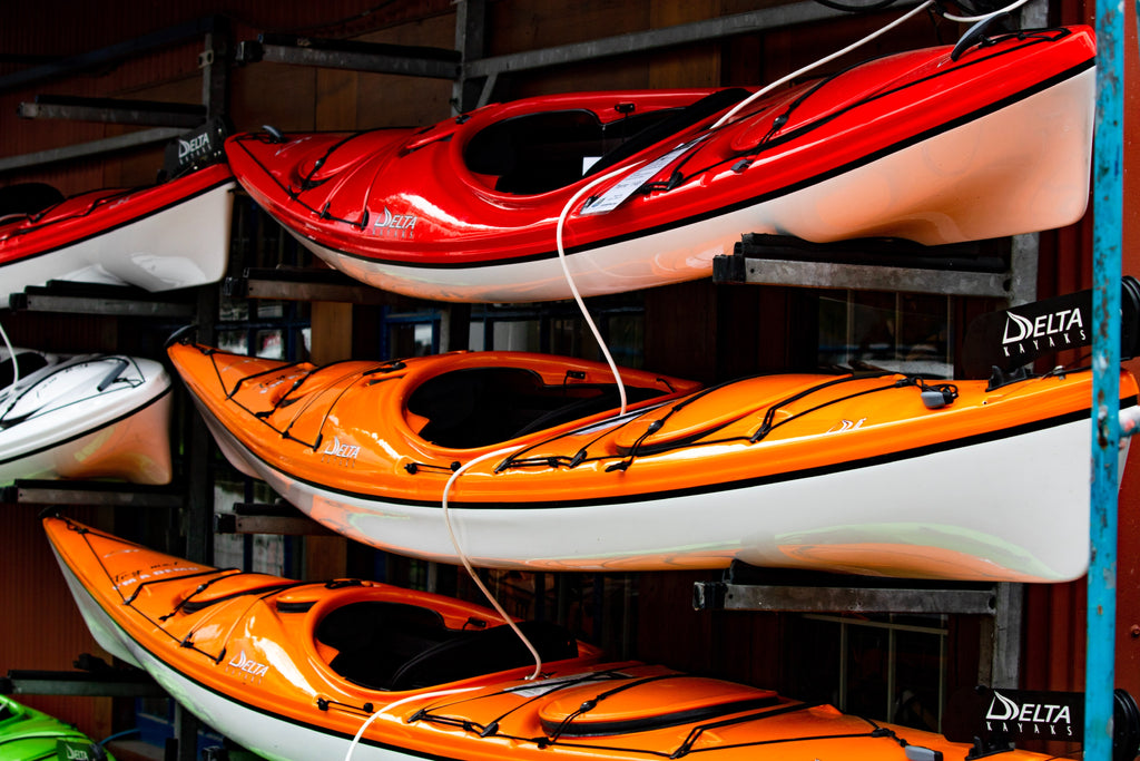 Orange and red kayaks that are stored on top of each other and are nicely cleaned. 