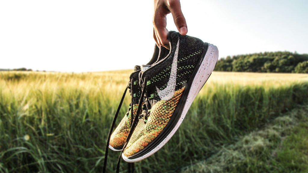 A pair of Nike running shoes that are being held in front of a scenic green field. 