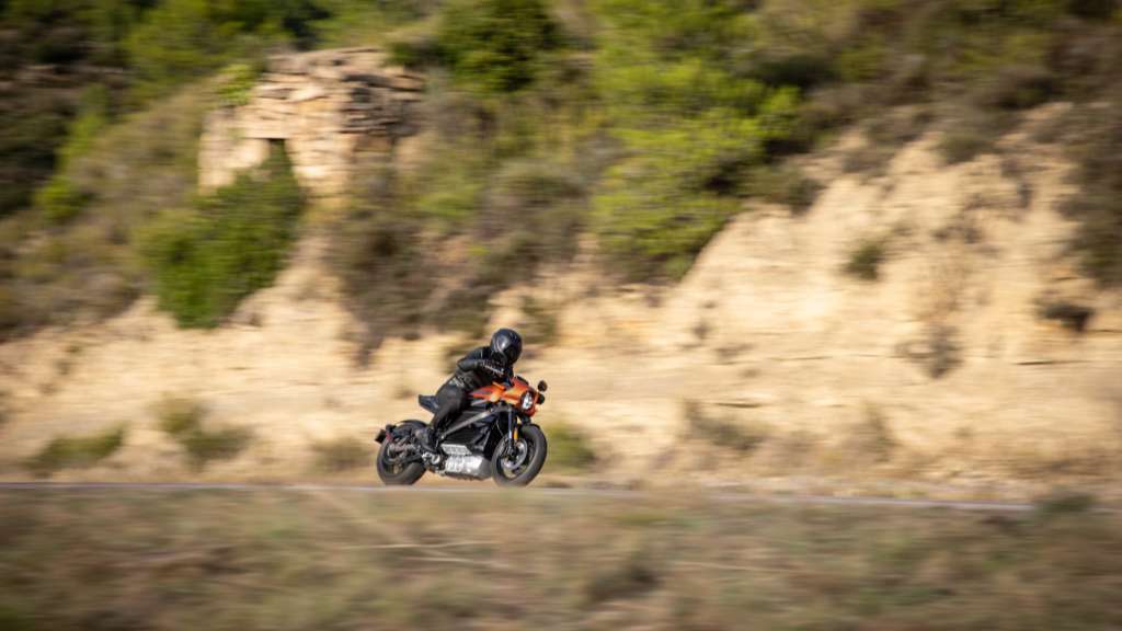 A man is riding a Harley-Davidson motorcycle at a pretty high speed on a narrow road