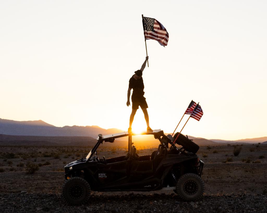 A man standing on Kemimoto Polaris RZR with flags waving