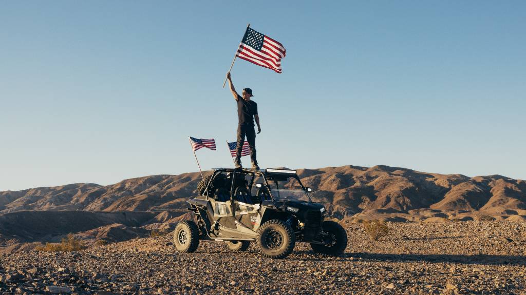 A man standing on Polaris RZR and waving flags-1